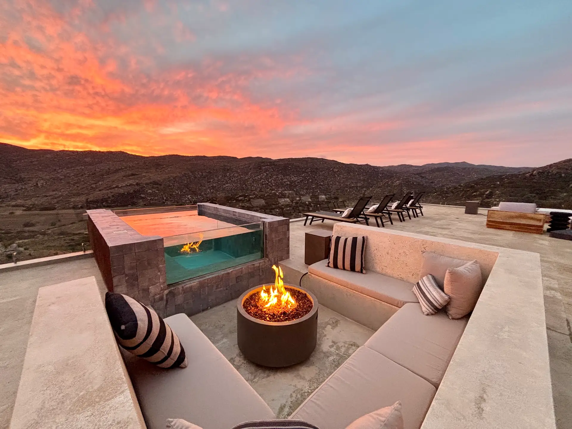 Sunken lounge with a fire pit beside the glass-walled plunge pool at sunset, Kasa Kefi